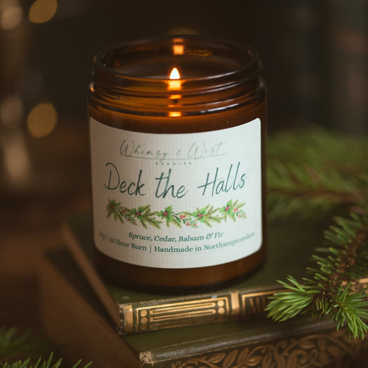 Lit Deck the Halls Christmas candle in an amber jar on vintage books with pine sprigs and fairy lights