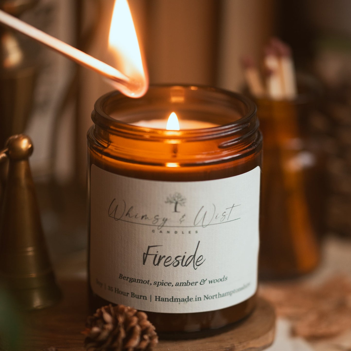 Candle labeled 'Fireside' from Whimsy & Wist on a wooden surface with a lit match