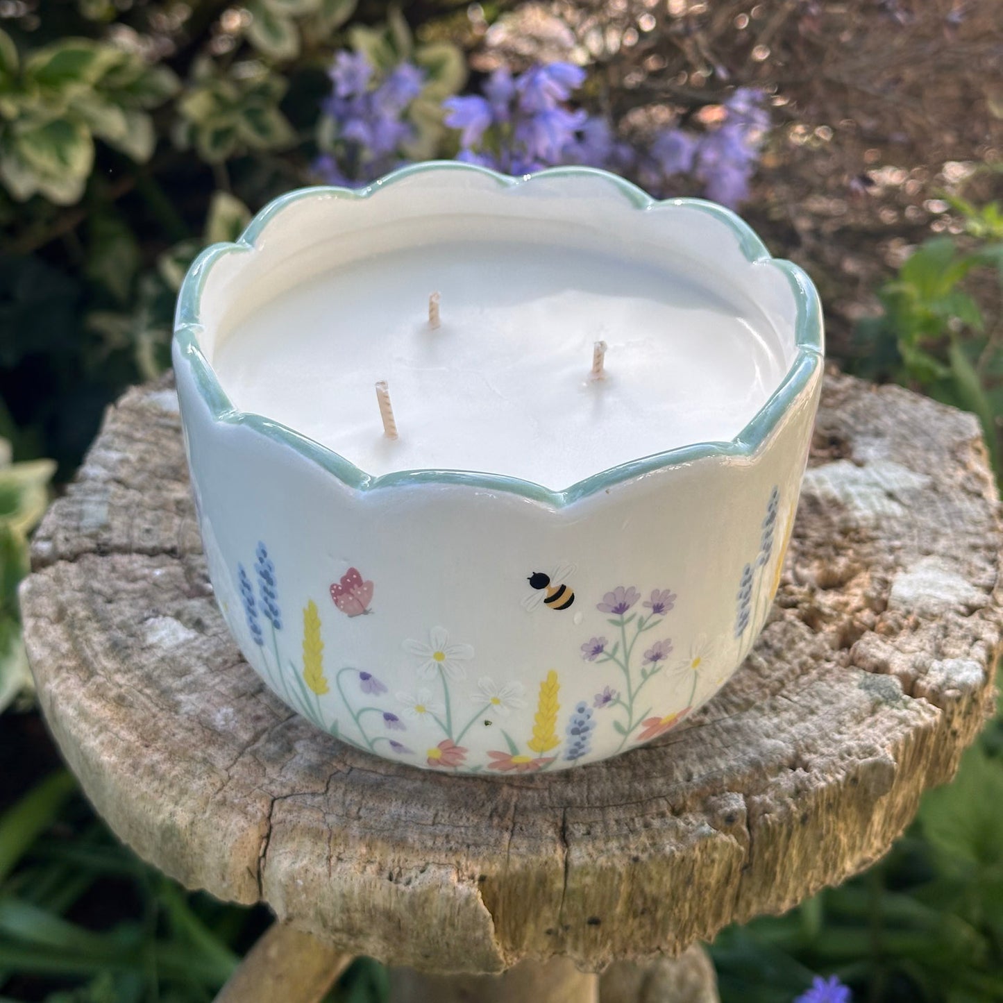 Decorative candle in a floral container on a wooden stand with a garden background
