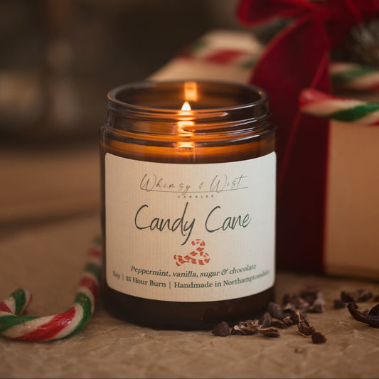 Lit Candy Cane peppermint candle in an amber jar with candy canes, cacao nibs and a gift tied in red ribbon