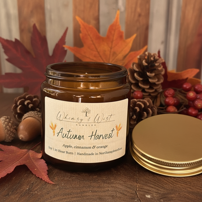 Candle jar labeled 'Autumn Harvest' with autumn themed decor on a wooden surface