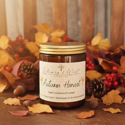 Candle labeled 'Autumn Harvest' surrounded by autumn themed decorations on a wooden surface.