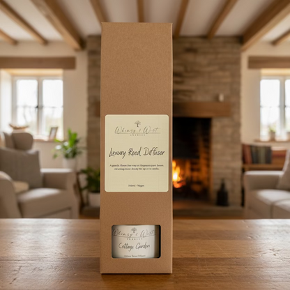 Whimsy & Wist Candles reed diffuser in a brown box on a wooden surface with a cottage background