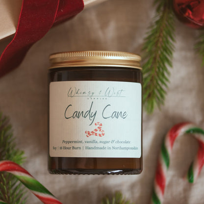 Whimsy & Wist Candy Cane soy candle with gold lid on cream linen with red and green candy canes and pine
