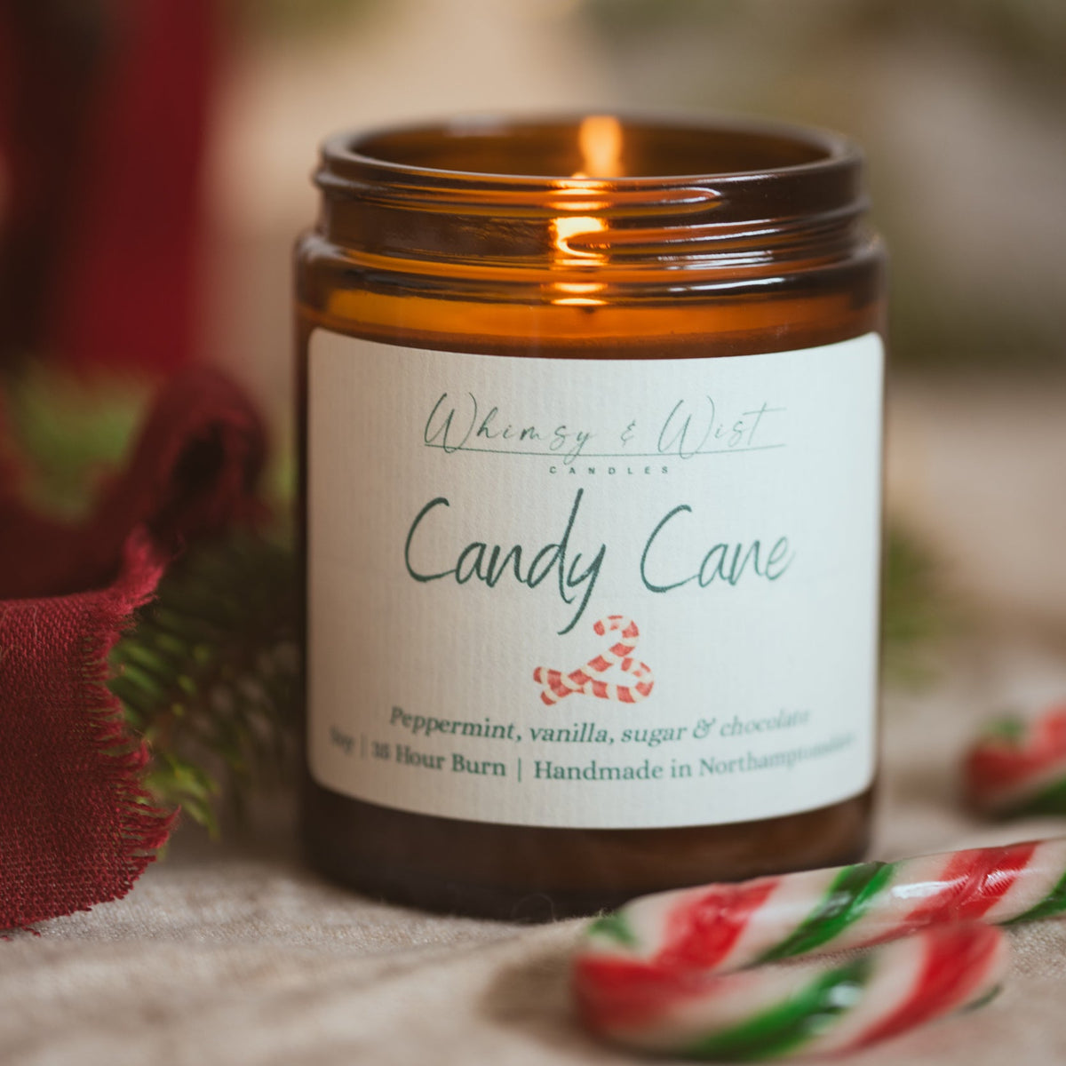 Lit Candy Cane soy candle on linen with red and green striped candy canes and red fabric