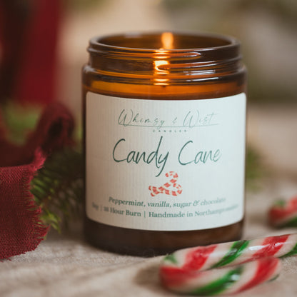 Lit Candy Cane soy candle on linen with red and green striped candy canes and red fabric