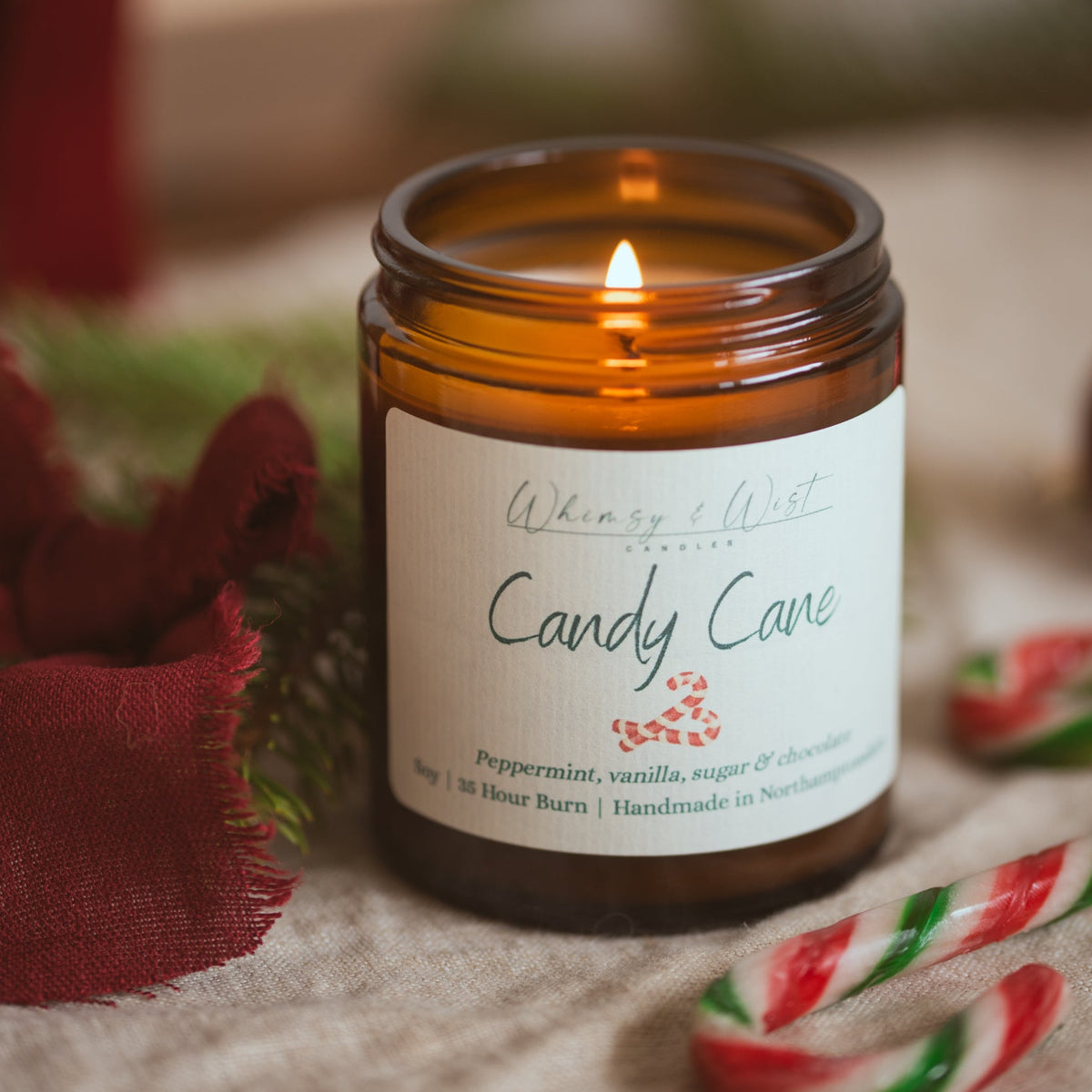 Lit Candy Cane soy candle showing the wax pool, with candy canes, pine and red linen