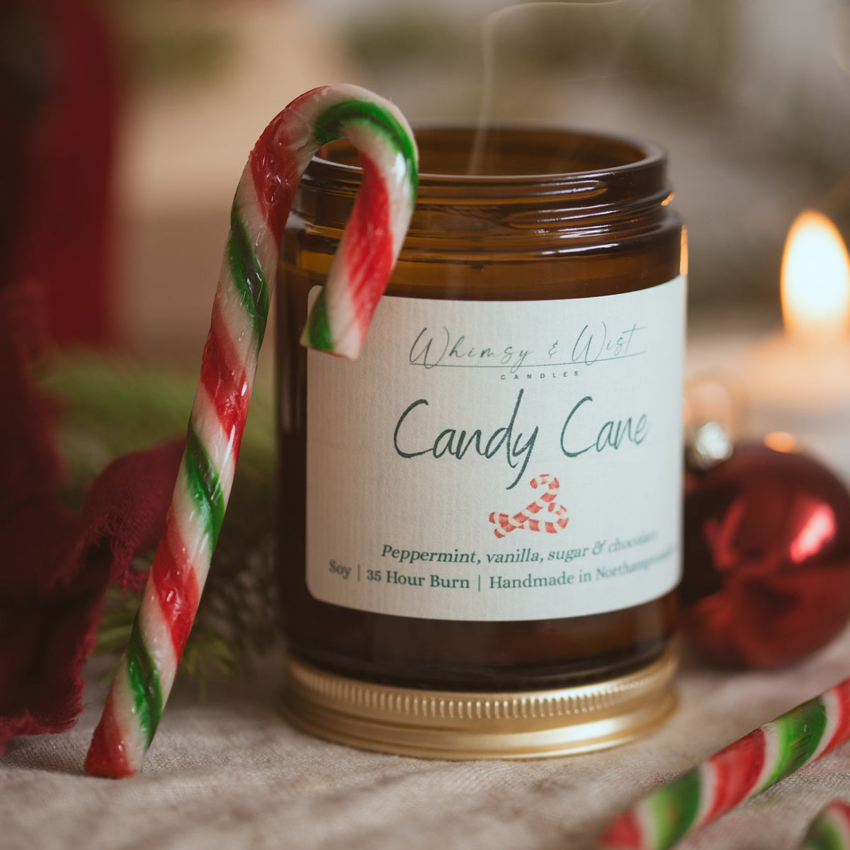 Candy Cane soy candle with a striped candy cane hooked over the jar and a wisp of smoke rising