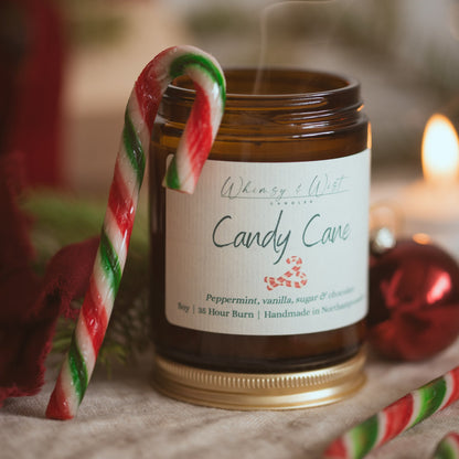 Candy Cane soy candle with a striped candy cane hooked over the jar and a wisp of smoke rising