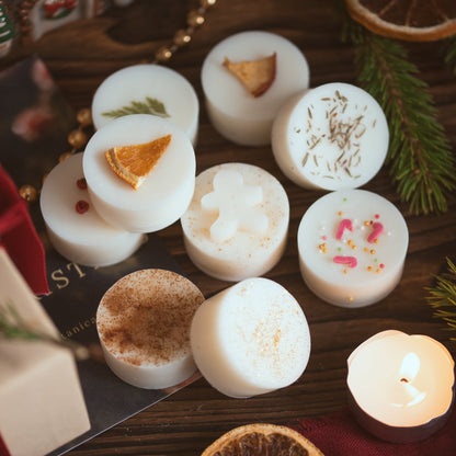 Nine 'Scents of Christmas' wax melts topped with dried orange, gingerbread men, candy canes, pine and spices, beside a lit tea light