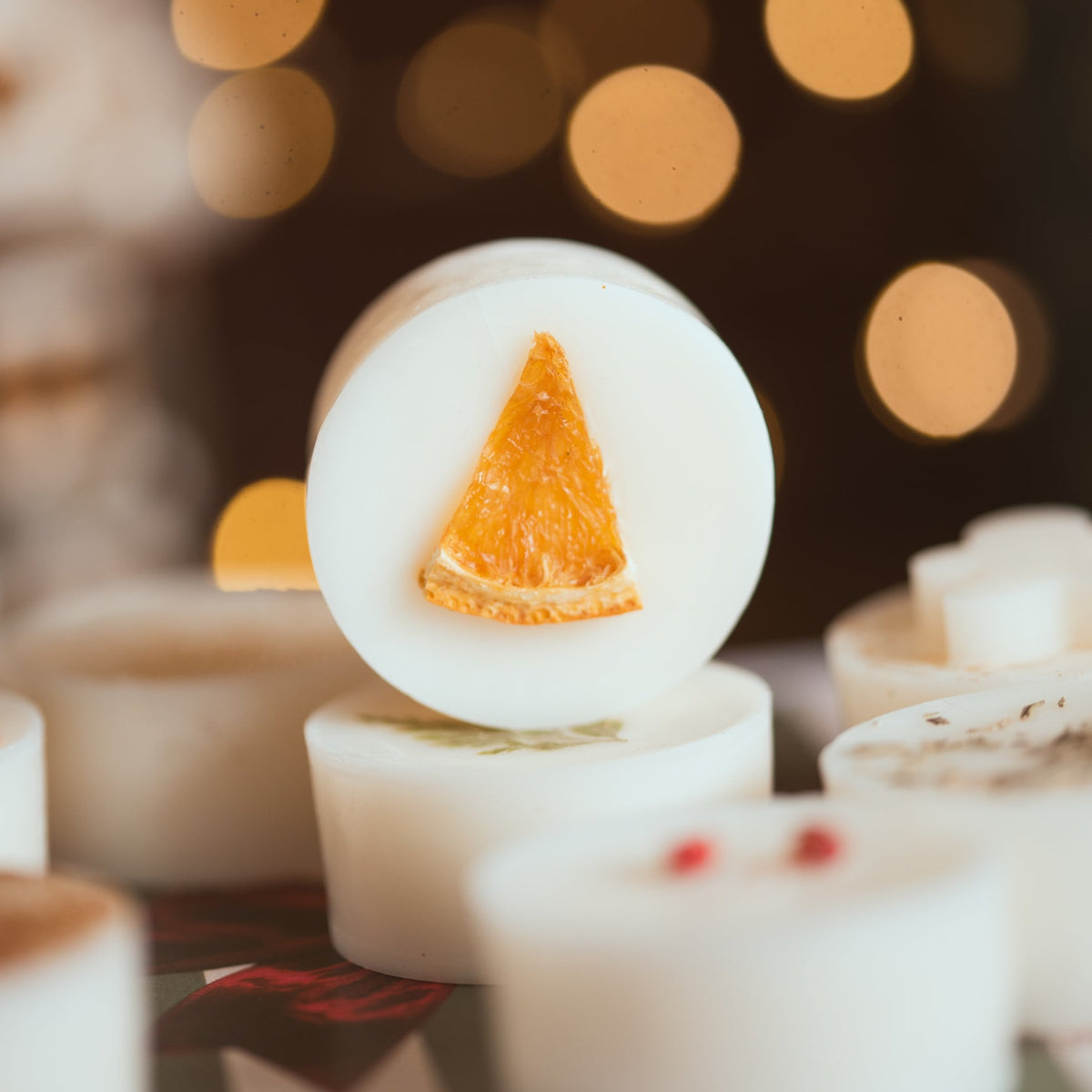 Close-up of a Christmas wax melt topped with a dried orange slice, with twinkling fairy lights behind