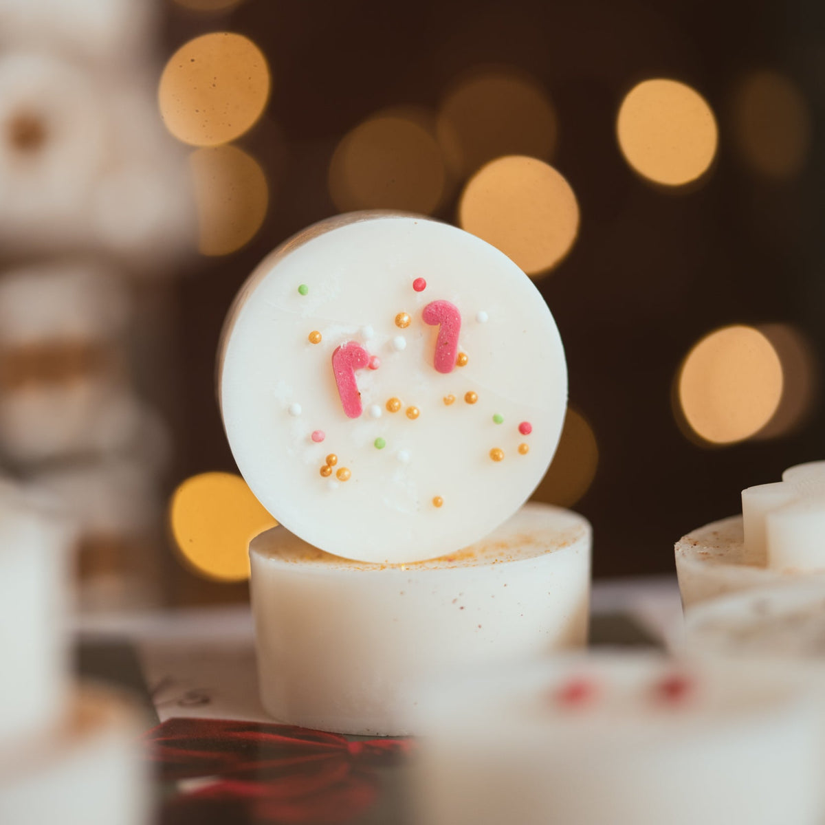 Close-up of a festive wax melt decorated with mini candy canes and sprinkles, with fairy lights behind