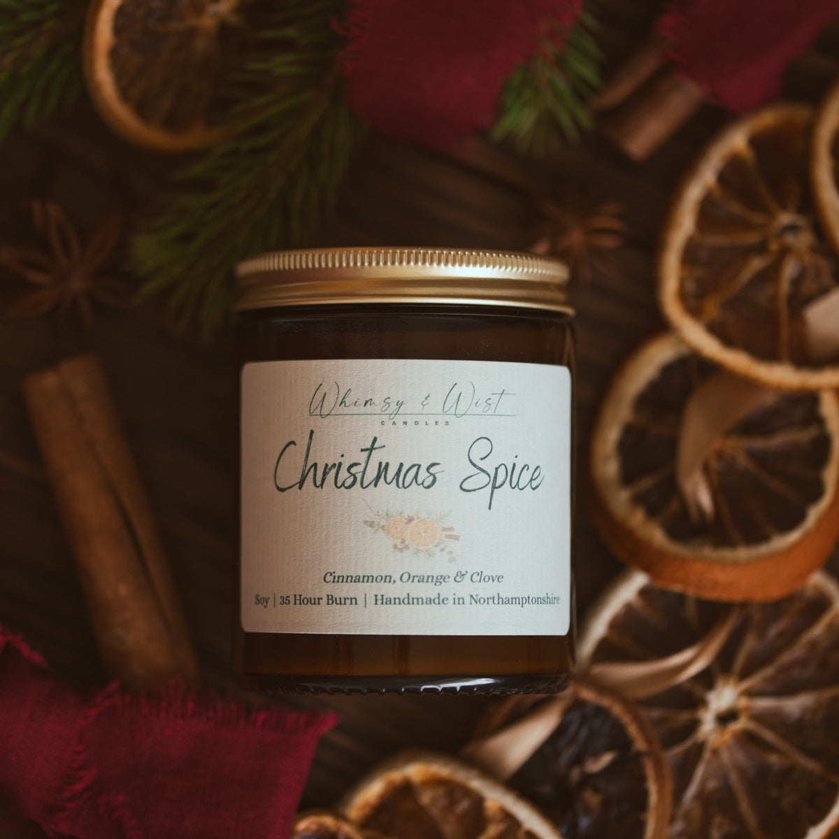 Whimsy & Wist Christmas Spice soy candle with gold lid among dried orange slices, cinnamon sticks and star anise
