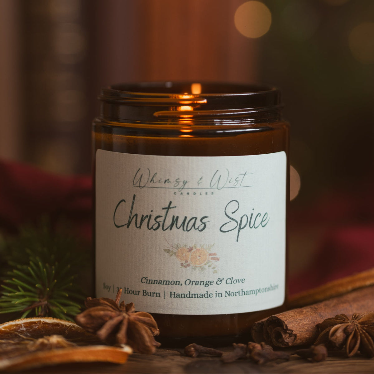 Lit Christmas Spice candle in an amber jar with cinnamon sticks, star anise, cloves and dried orange