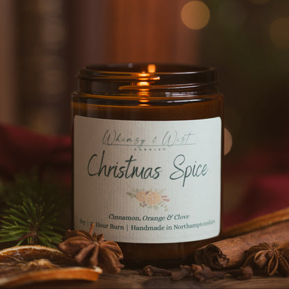 Lit Christmas Spice candle in an amber jar with cinnamon sticks, star anise, cloves and dried orange