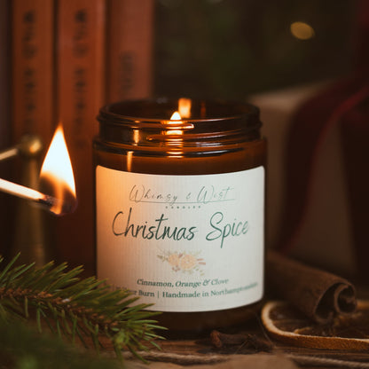 Christmas Spice soy candle being lit with a match, with pine, cinnamon and dried orange slices