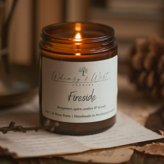 Candle in a amber jar labeled 'Fireside' by 'Whimsy & Wist' on a rustic background.