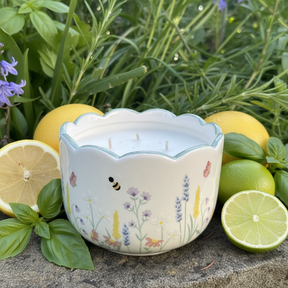 Decorative candle with floral design surrounded by lemons and limes on a stone surface.