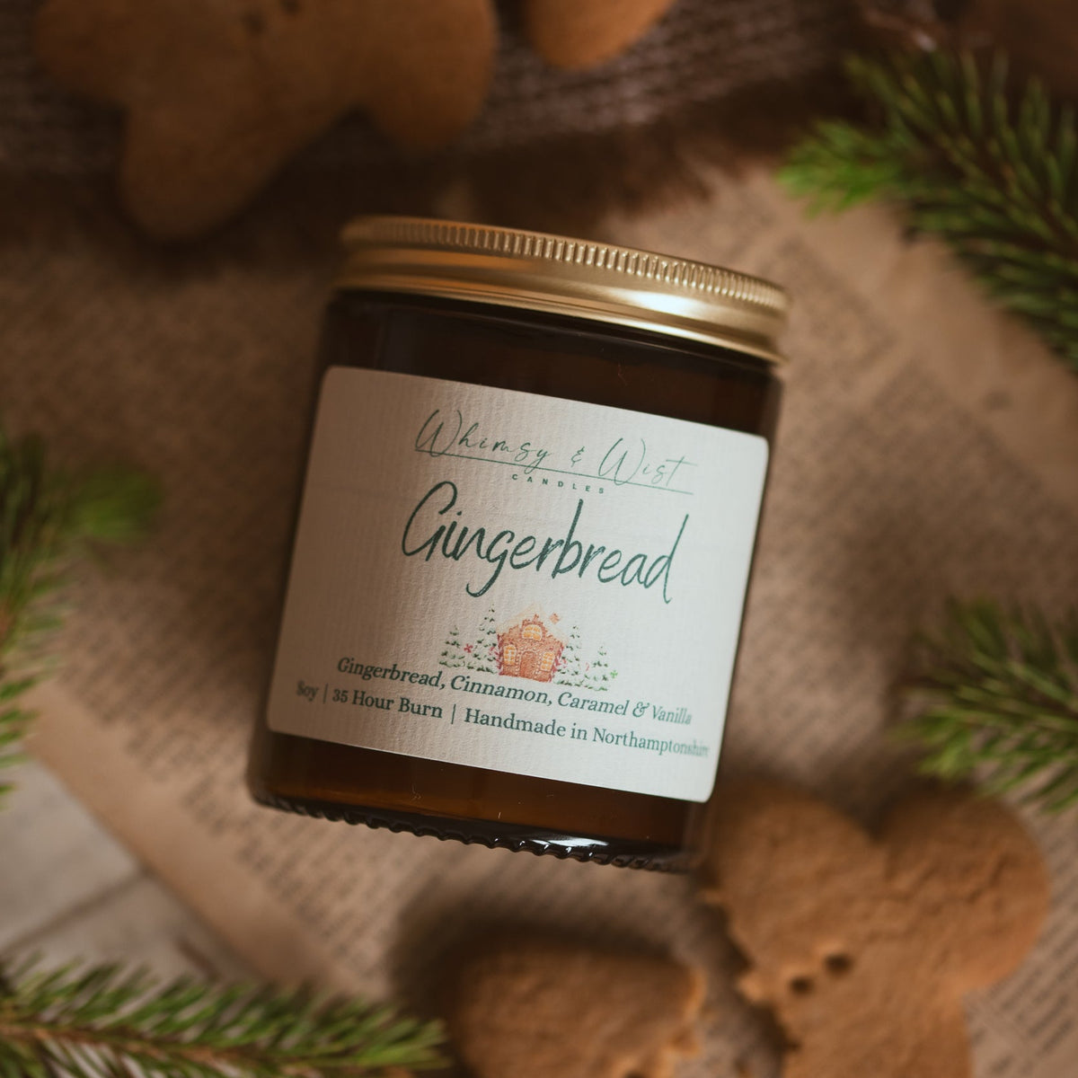 Whimsy & Wist Gingerbread soy candle in an amber jar with gold lid, on hessian with gingerbread biscuits and pine