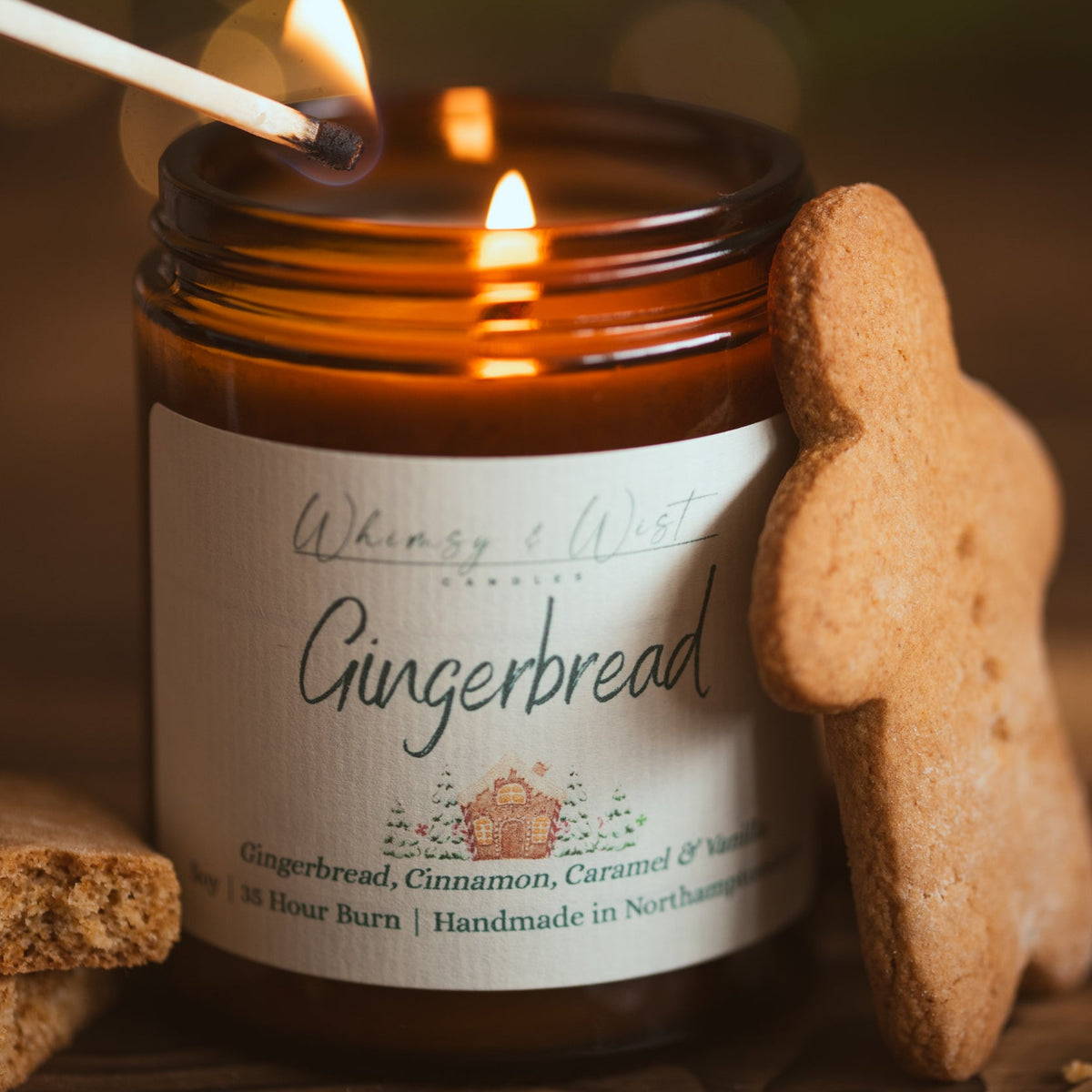 Gingerbread soy candle being lit with a match, with a gingerbread man biscuit leaning against the jar