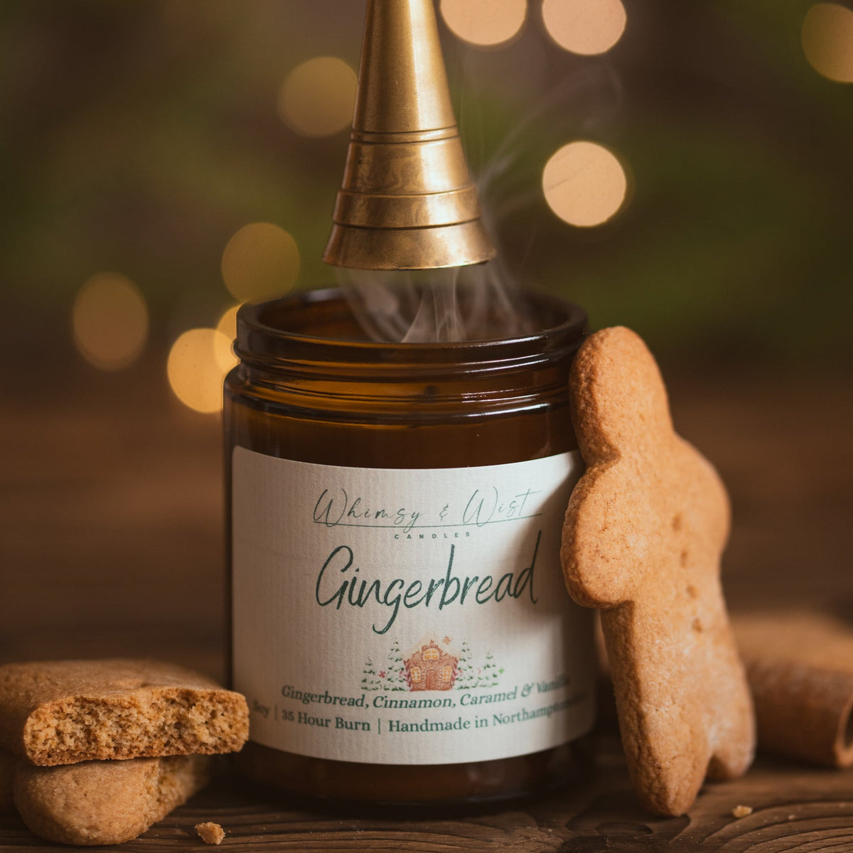 Gingerbread soy candle being put out with a brass snuffer, with a gingerbread man biscuit beside it