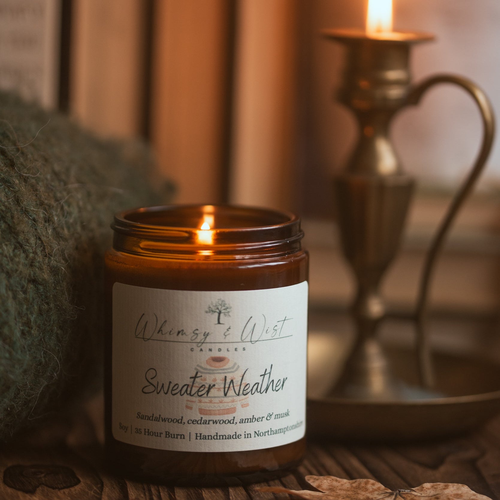 Candle labeled 'Sweater Weather' on a wooden surface with a blurred background