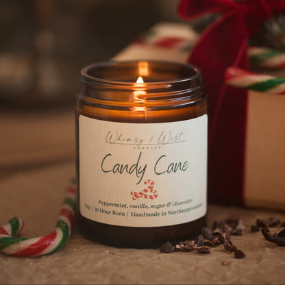 Lit Candy Cane peppermint candle in an amber jar with candy canes, cacao nibs and a gift tied in red ribbon