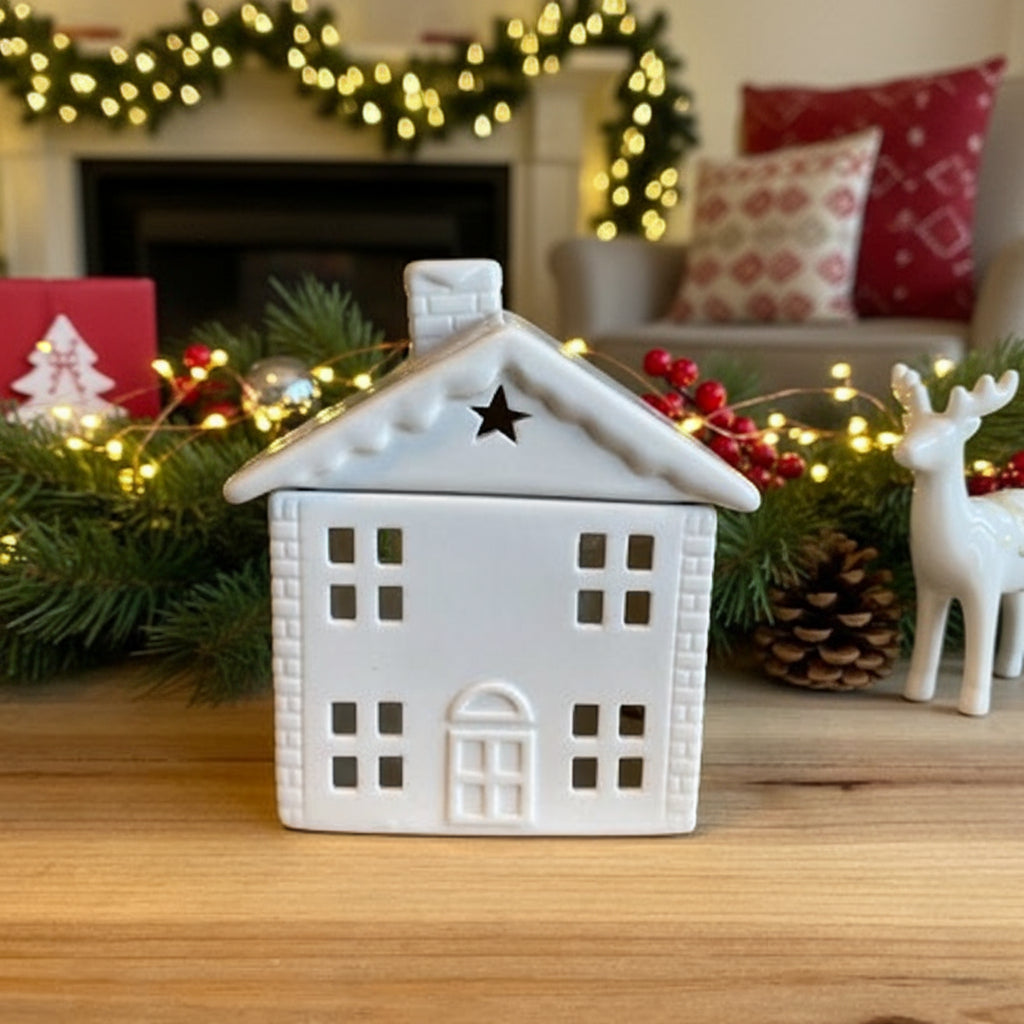 White ceramic house-shaped burner on a wooden surface with a Christmas background