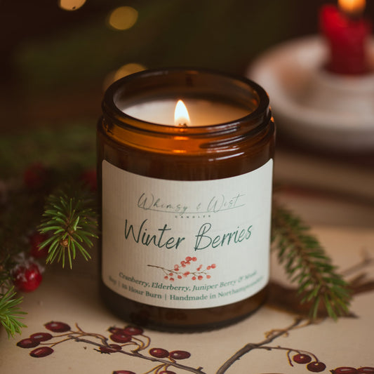 Lit Winter Berries Christmas candle in an amber jar with pine sprigs and red berries on a botanical berry print