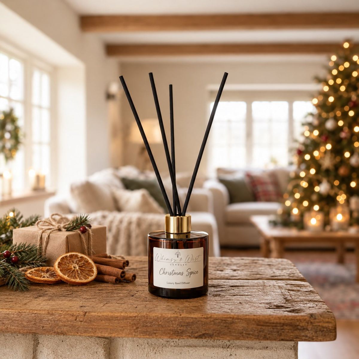 Whimsy & Wist Christmas Spice reed diffuser on a rustic table with cinnamon, dried orange and a Christmas tree behind