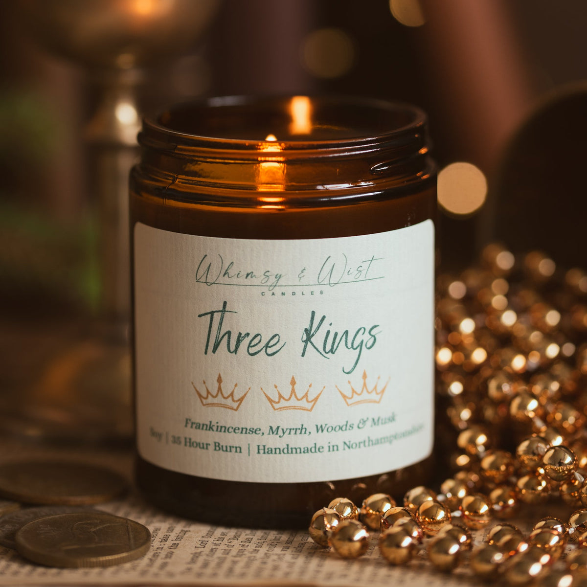 Lit Three Kings Christmas candle in an amber jar with strings of gold beads and an antique coin