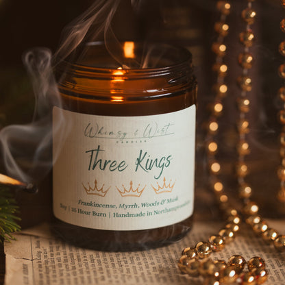 Three Kings soy candle with wisps of smoke curling up beside it, surrounded by gold beads
