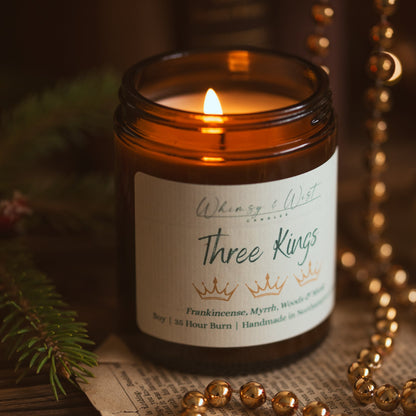 Lit Three Kings soy candle showing the wax pool, with gold beads, pine and vintage book pages